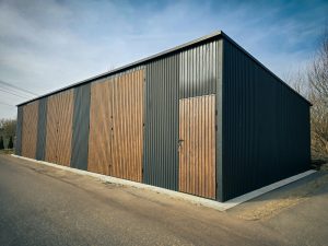 Fémgarázs / Acélcsarnok 15×7 m, három kétszárnyú kapuval és egy személybejáró ajtóval, fekete + dió színben, Pluto modell
